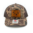 A camouflage trucker hat with a brown leather patch on the front and a white size sticker on the brim, photographed against a plain white background.