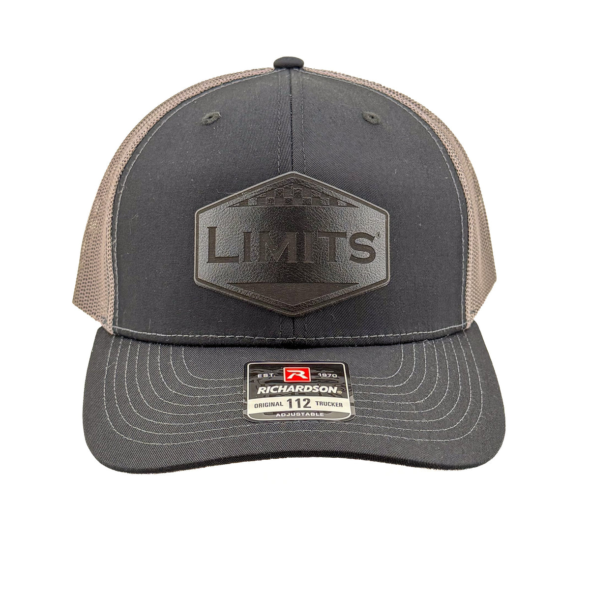 A Richardson 112 trucker hat in black and charcoal grey mesh, featuring a black hexagonal patch on the front with the word 'LIMITS' and a Richardson brand sticker on the visor.