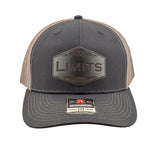 A Richardson 112 trucker hat in black and charcoal grey mesh, featuring a black hexagonal patch on the front with the word 'LIMITS' and a Richardson brand sticker on the visor.