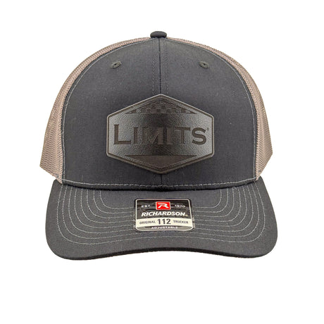 A Richardson 112 trucker hat in black and charcoal grey mesh, featuring a black hexagonal patch on the front with the word 'LIMITS' and a Richardson brand sticker on the visor.