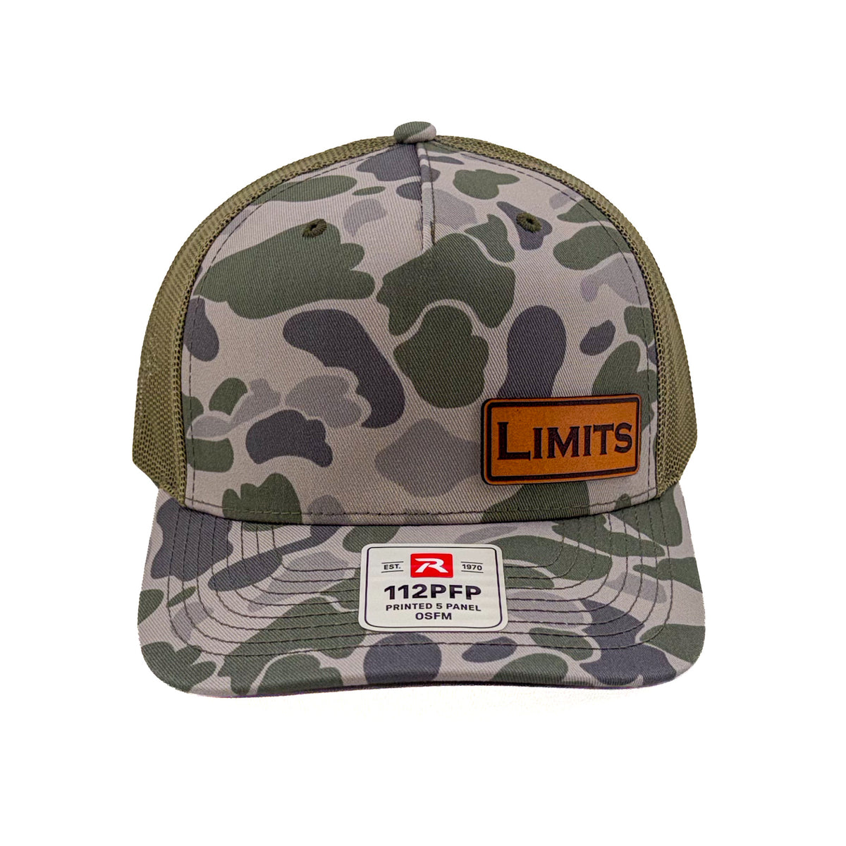 A camouflage trucker hat with green and gray camo print on the front panel and brim, olive mesh back panels, and a brown leather patch on the front with the brand name 'LIMITS'.